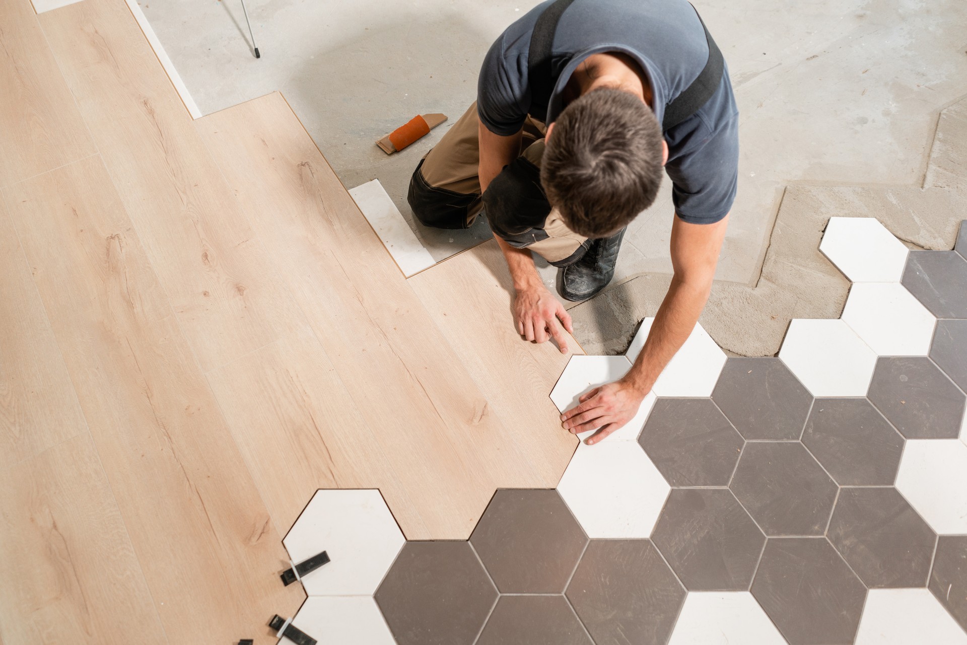 Artisan qui installe nouveau parquet stratifié. La combinaison de panneaux de stratifié et céramique carreaux en forme de nid d’abeilles. Rénovation de la cuisine.