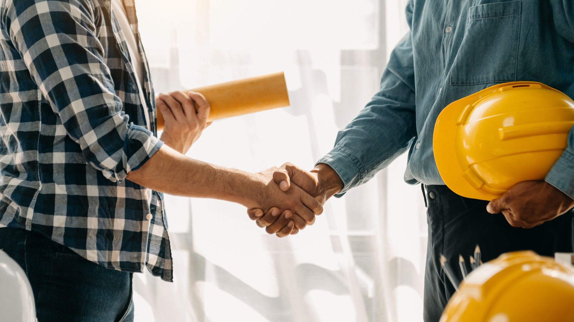 L’équipe de construction se serre la main pour commencer le nouveau plan de projet derrière le casque jaune sur le bureau dans le centre de bureau pour consulter sur leur projet de construction.